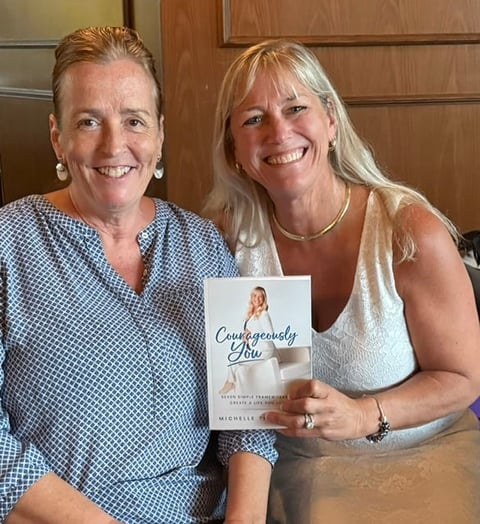 Two women smiling at camera while holding a book titled Courageously Abe indoors
