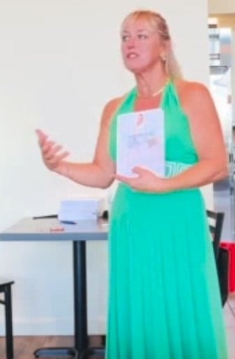 Woman in green dress and orange cardigan gesturing while speaking in an indoor office setting